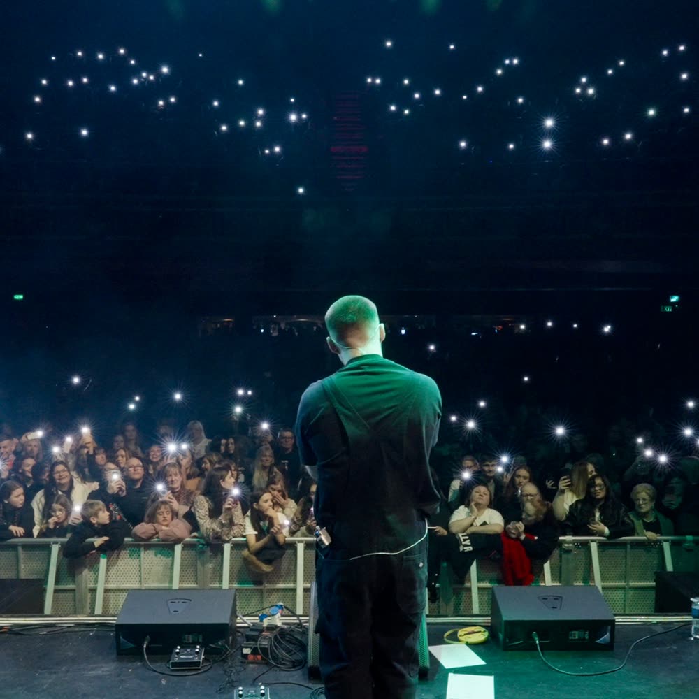 Roman Ellis on stage facing a crowd holding phone lights